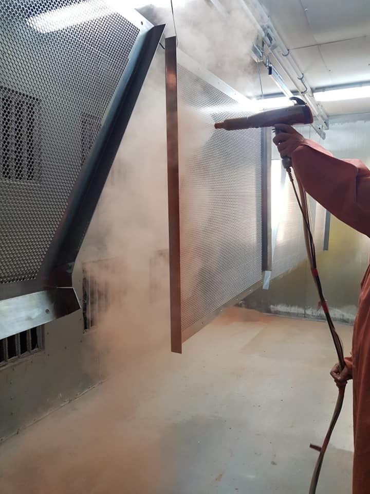 A Man Is Spraying Powder Paint On A Wall In A Room — Border Security Doors & Powder Coating in Albury, NSW