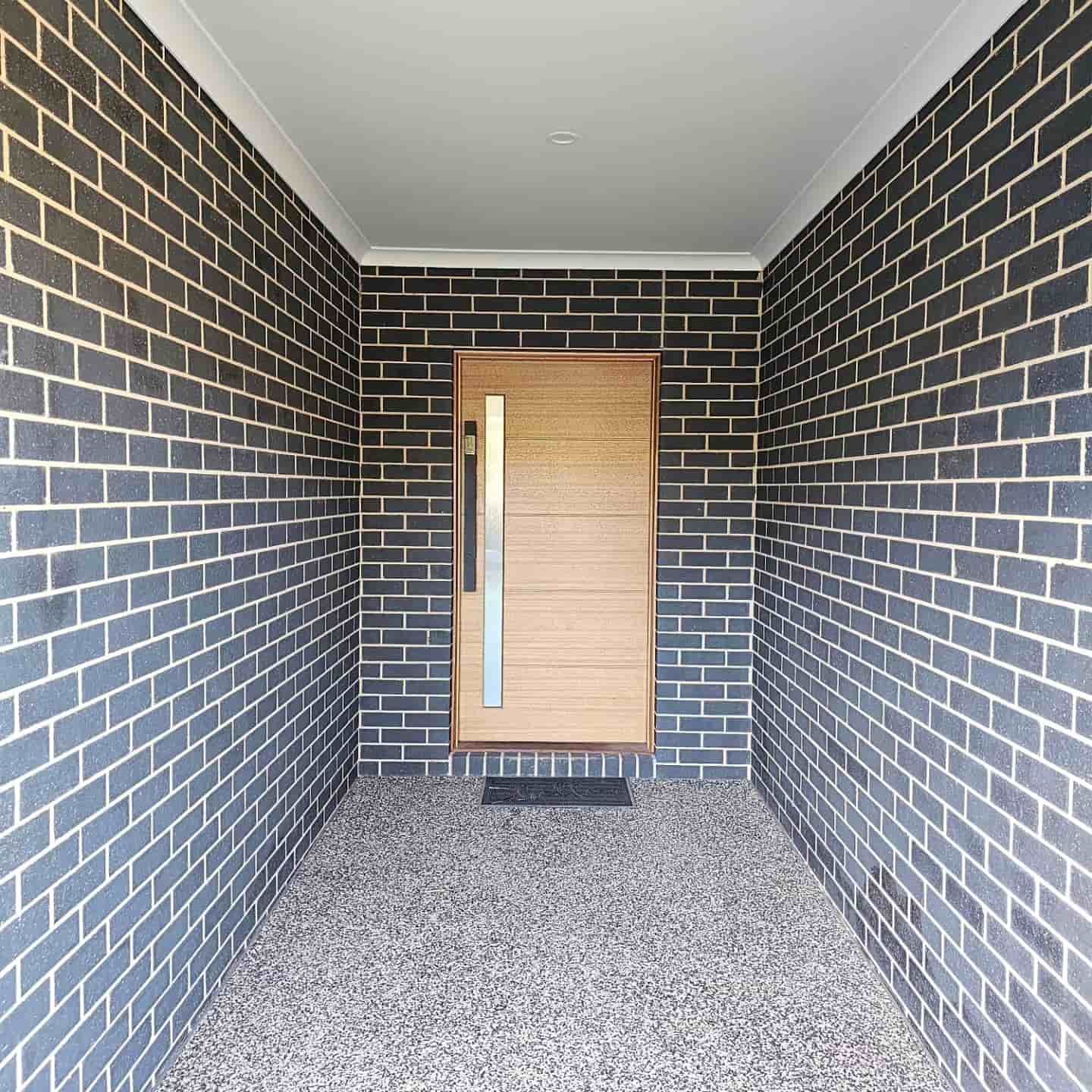 A Long Hallway With Brick Walls And A Wooden Door — Border Security Doors & Powder Coating in Wodonga, VIC