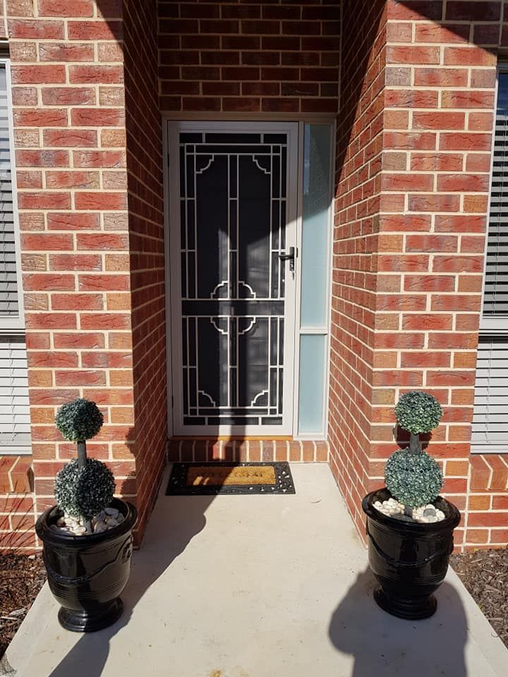 A Brick House With Two Potted Plants In Front Of It — Border Security Doors & Powder Coating in Wodonga, VIC