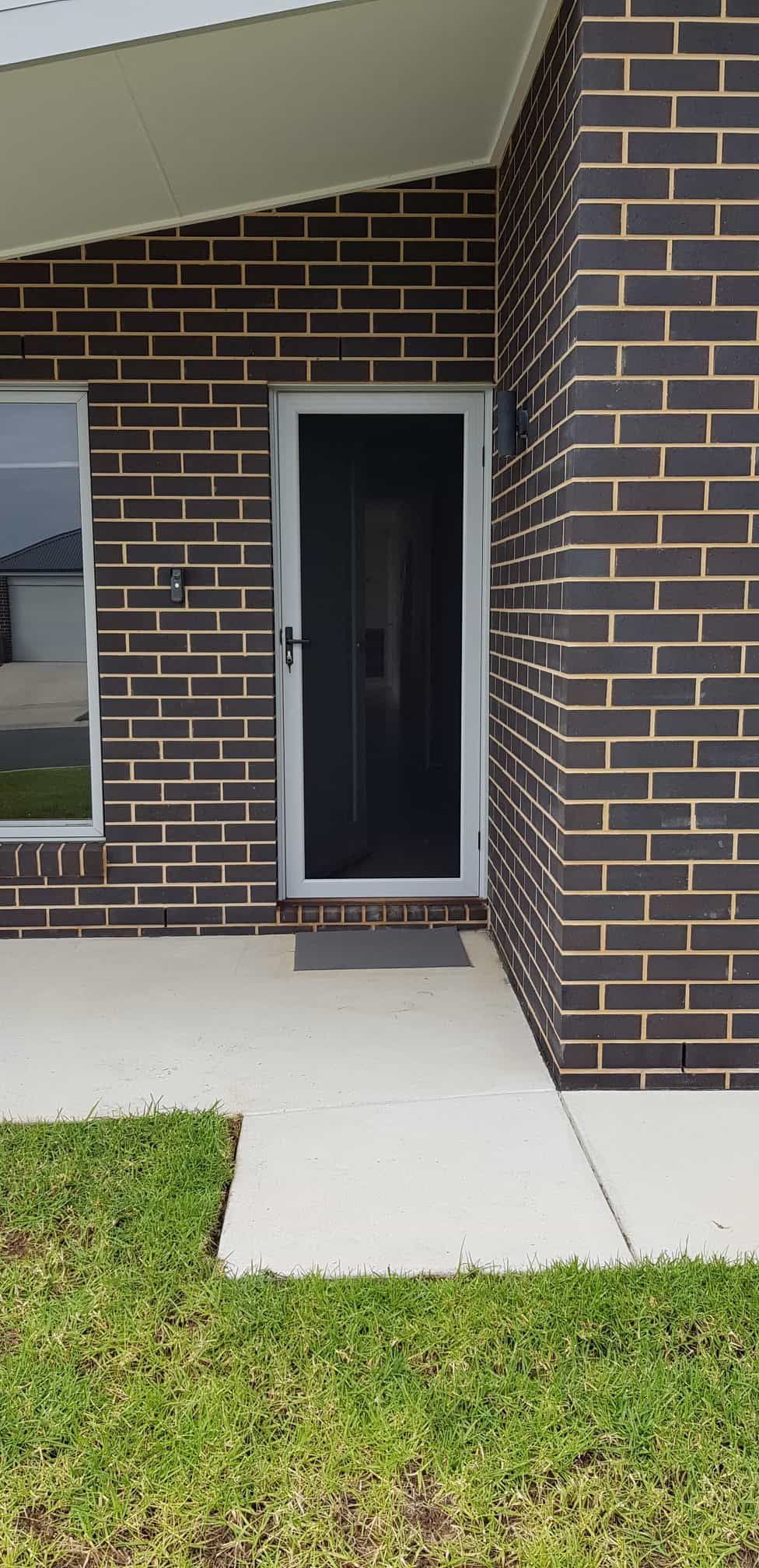 The Front Door Of A Brick House With A Screen Door — Border Security Doors & Powder Coating in Wodonga, VIC