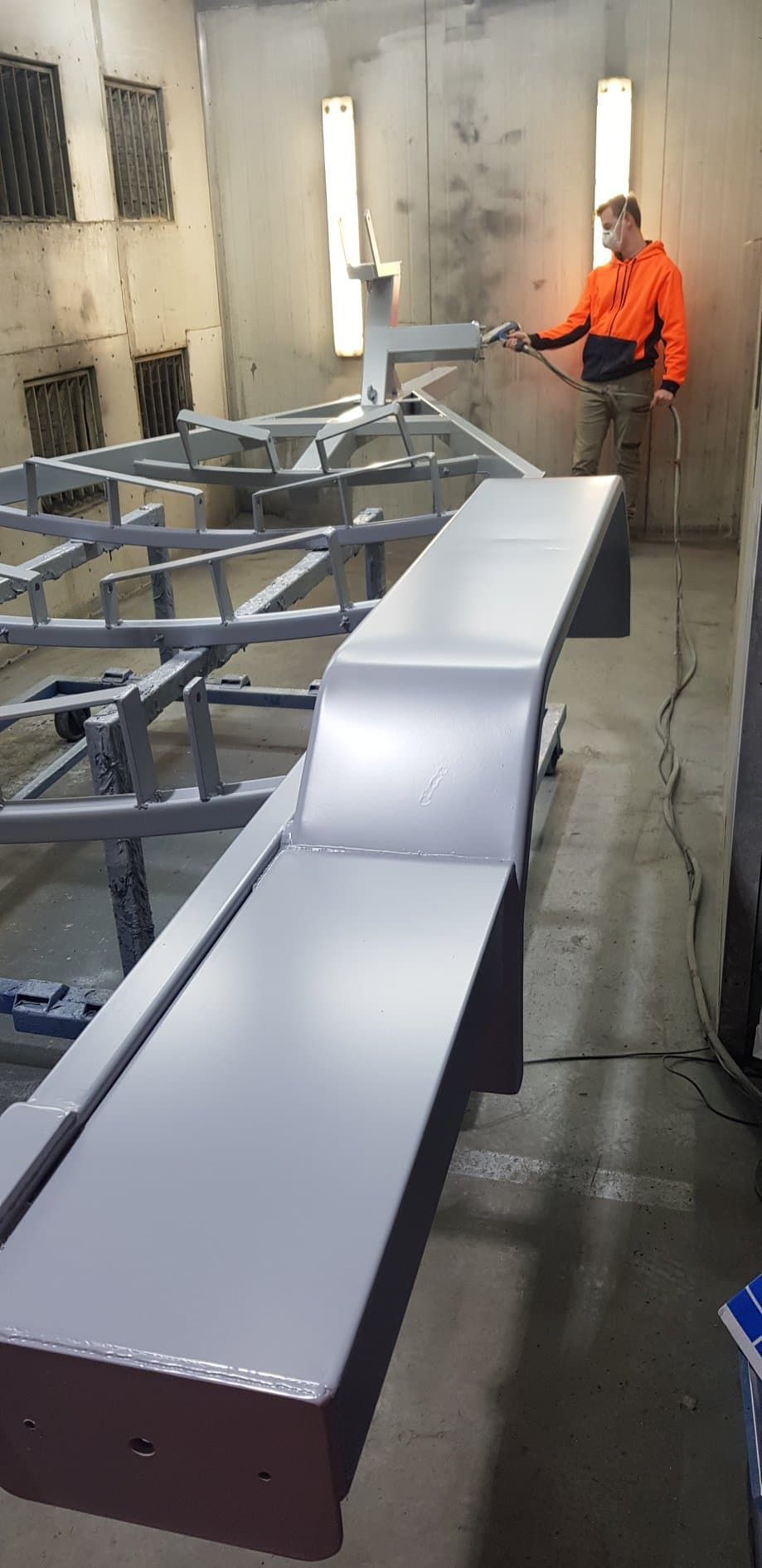 A Man Is Painting A Metal Structure In A Paint Booth — Border Security Doors & Powder Coating in Wangaratta, NSW