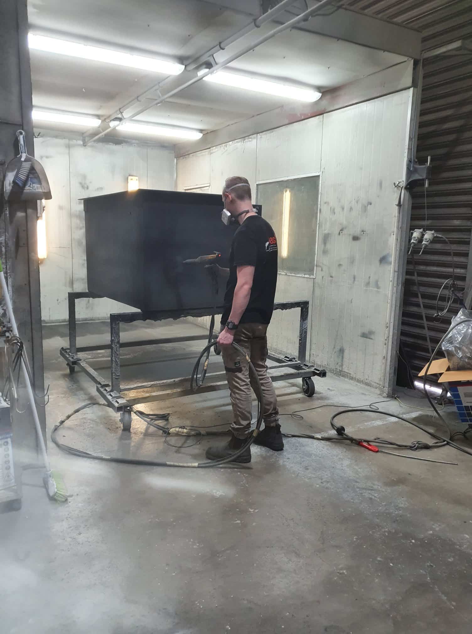 A Man Is Standing In A Room Holding A Welding Machine — Border Security Doors & Powder Coating in Wodonga, VIC