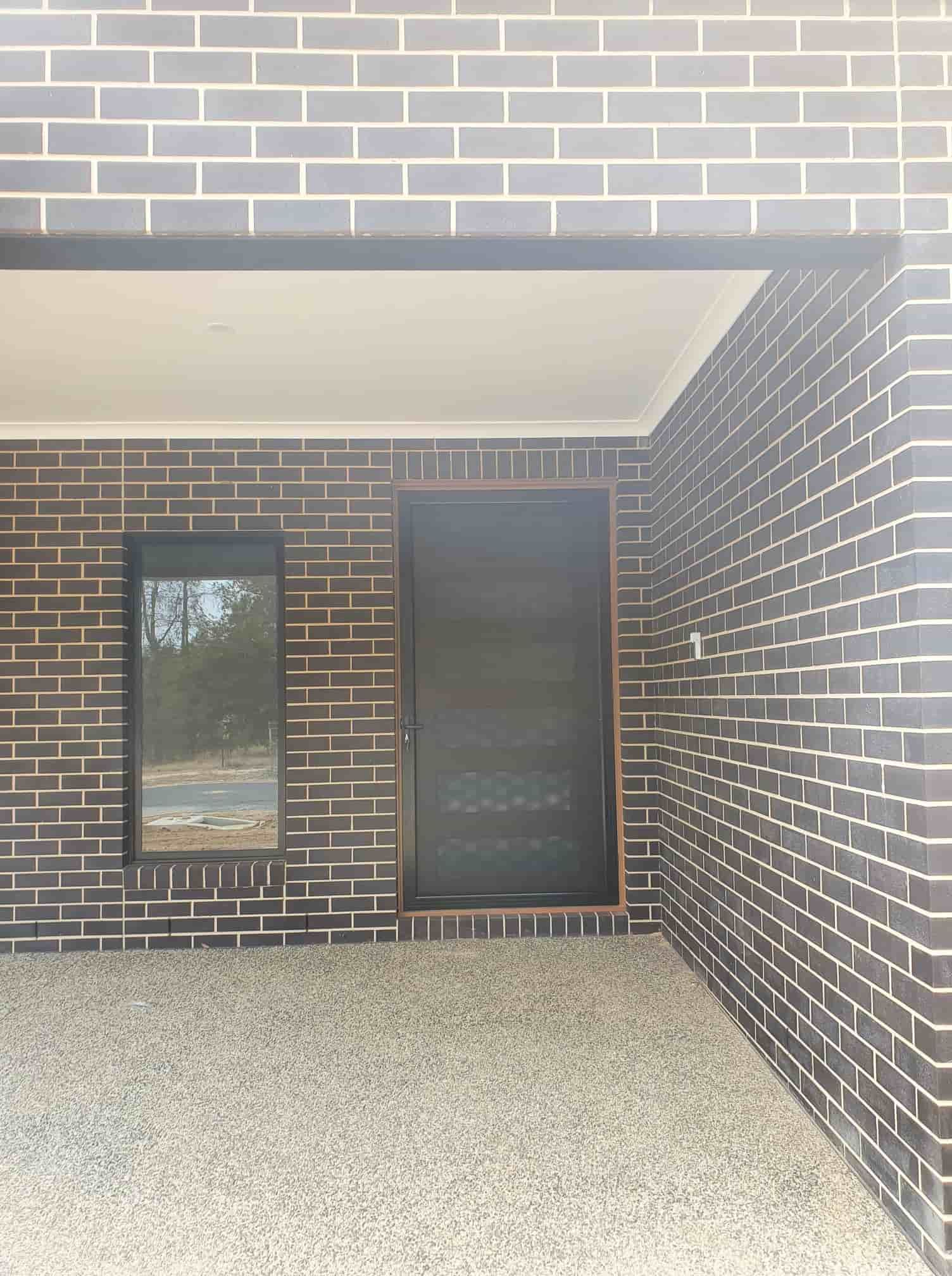 A Brick Building With A Black Door And A Window — Border Security Doors & Powder Coating in Wodonga, VIC