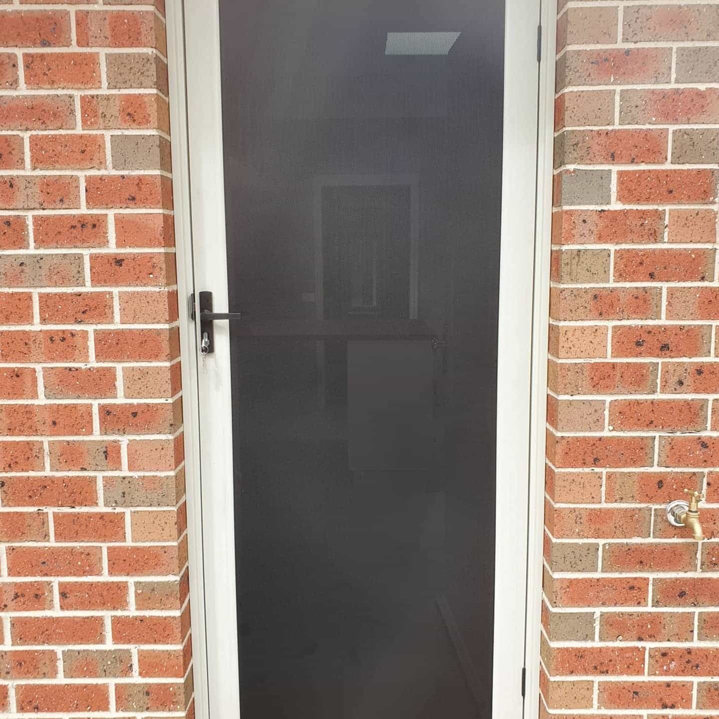 A White Screen Door Is On A Brick Wall — Border Security Doors & Powder Coating in Wodonga, VIC