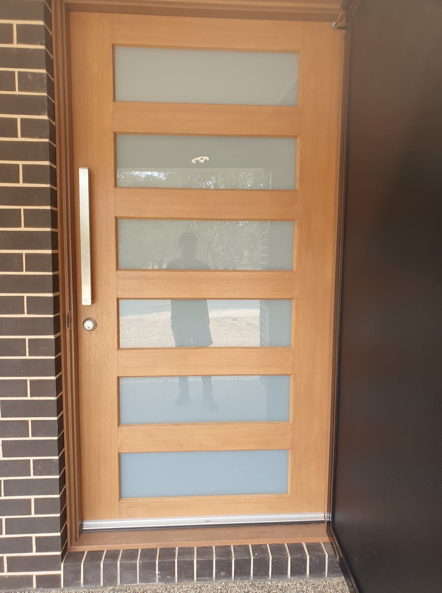 A Wooden Door With A Brick Wall Behind It — Border Security Doors & Powder Coating in Wodonga, VIC
