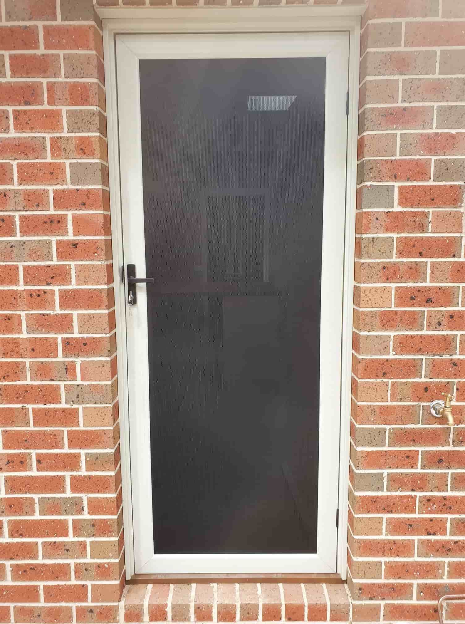A White Screen Door Is On A Red Brick Wall — Border Security Doors & Powder Coating in Wodonga, VIC