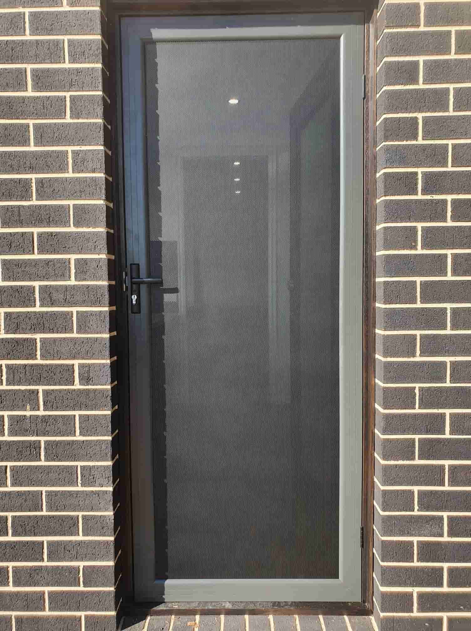 A Door With A Screen On It Is Against A Brick Wall — Border Security Doors & Powder Coating in Wodonga, VIC