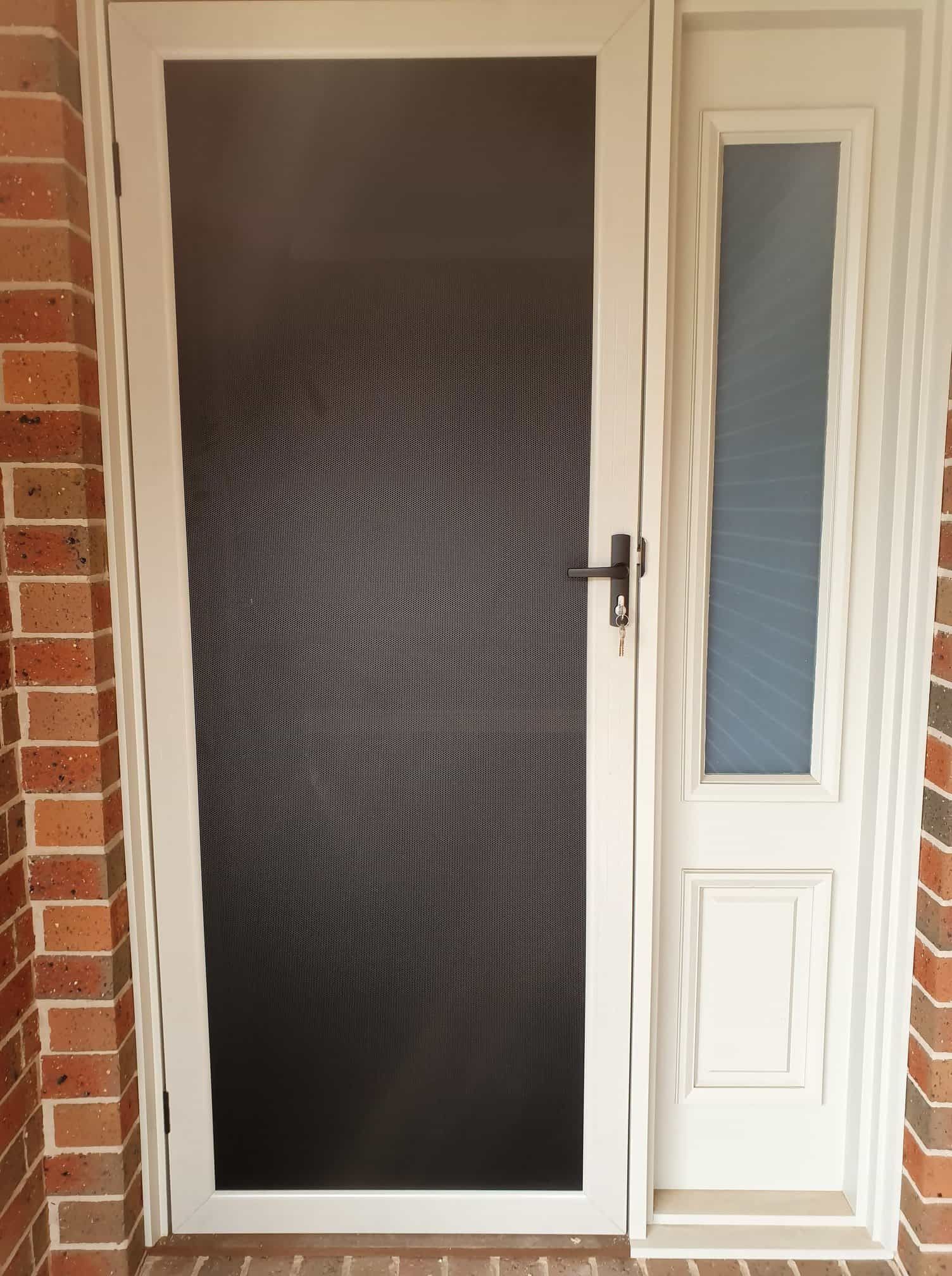 A White Screen Door With A Brick Wall In The Background — Border Security Doors & Powder Coating in Wodonga, VIC