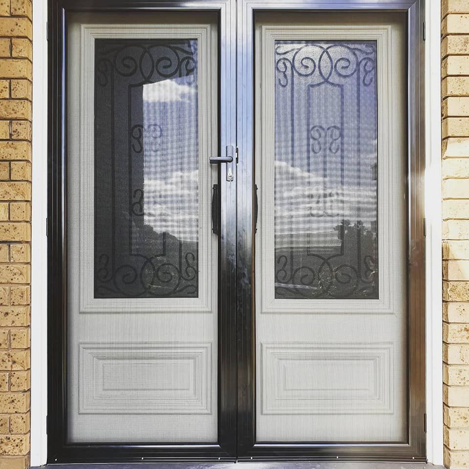 On A Brick Building, A White Door With A Wrought Iron Frame Is Situated — Border Security Doors & Powder Coating in Wodonga, VIC