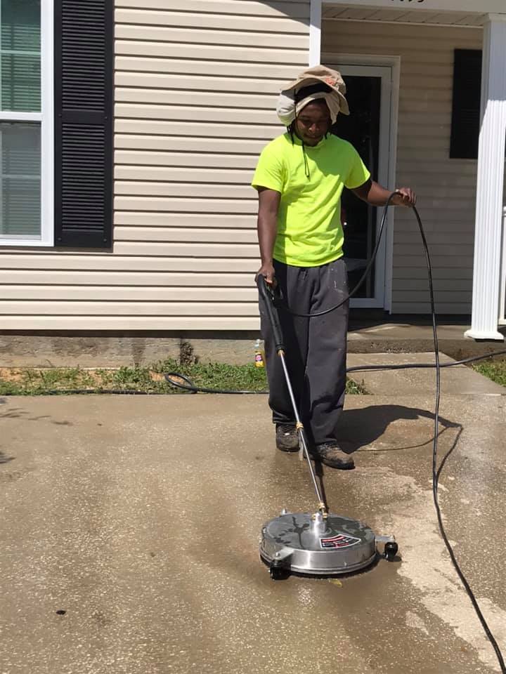 Man pressure washing a concrete driveway outside a house.