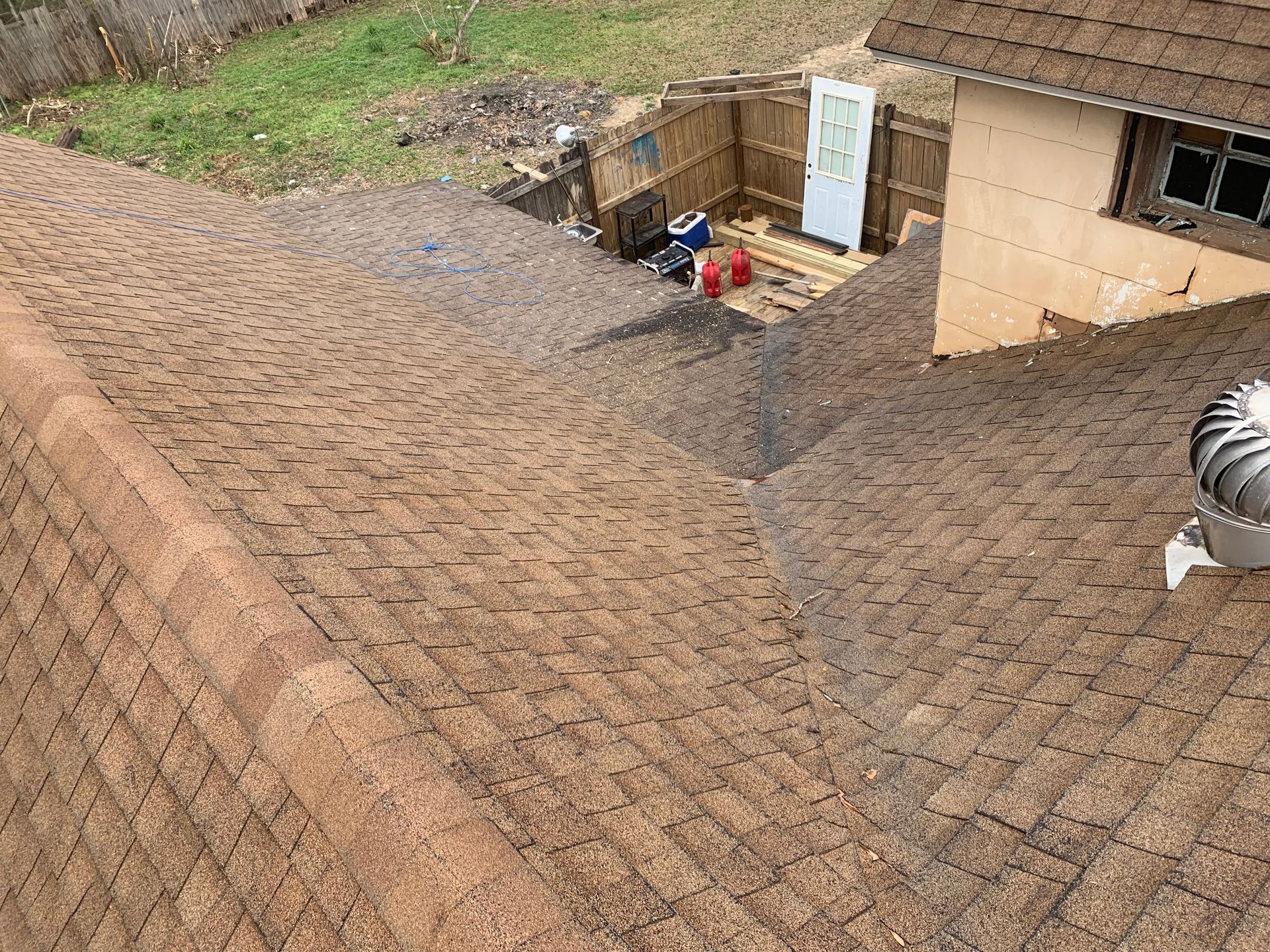Brown shingled roof, with a side view of a yard and a building with an open door.