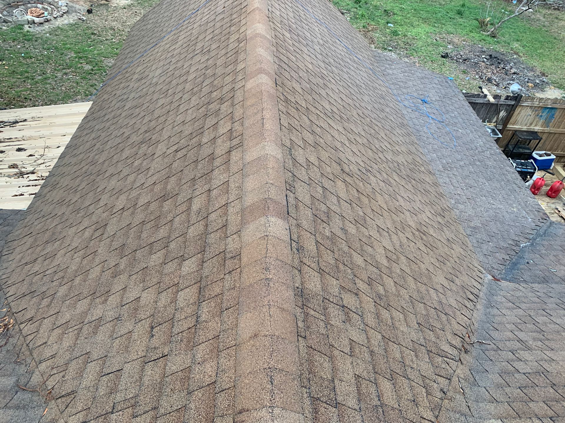 Overhead view of a brown shingled roof with a central ridge, set outside with greenery in the background.