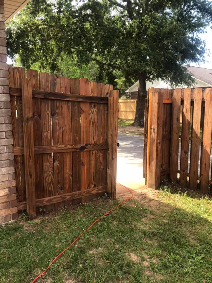 Wooden gate, stained brown, partially open in a backyard with green grass and brick wall.
