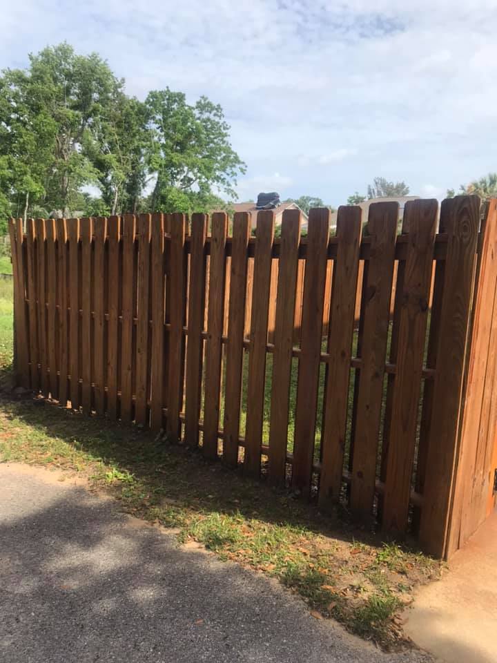 Wooden fence, brown color, on green grass with a paved area in front.
