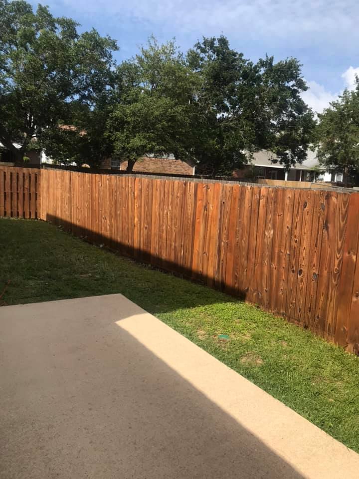 Backyard with a stained wooden fence and a concrete patio, with grass in between.