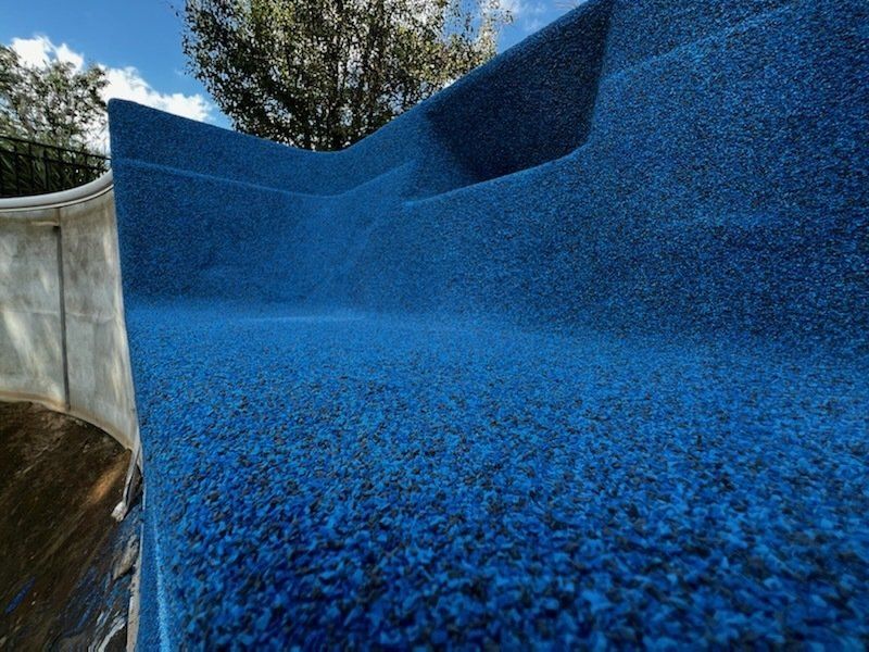 A close up of a blue slide in a pool with trees in the background.