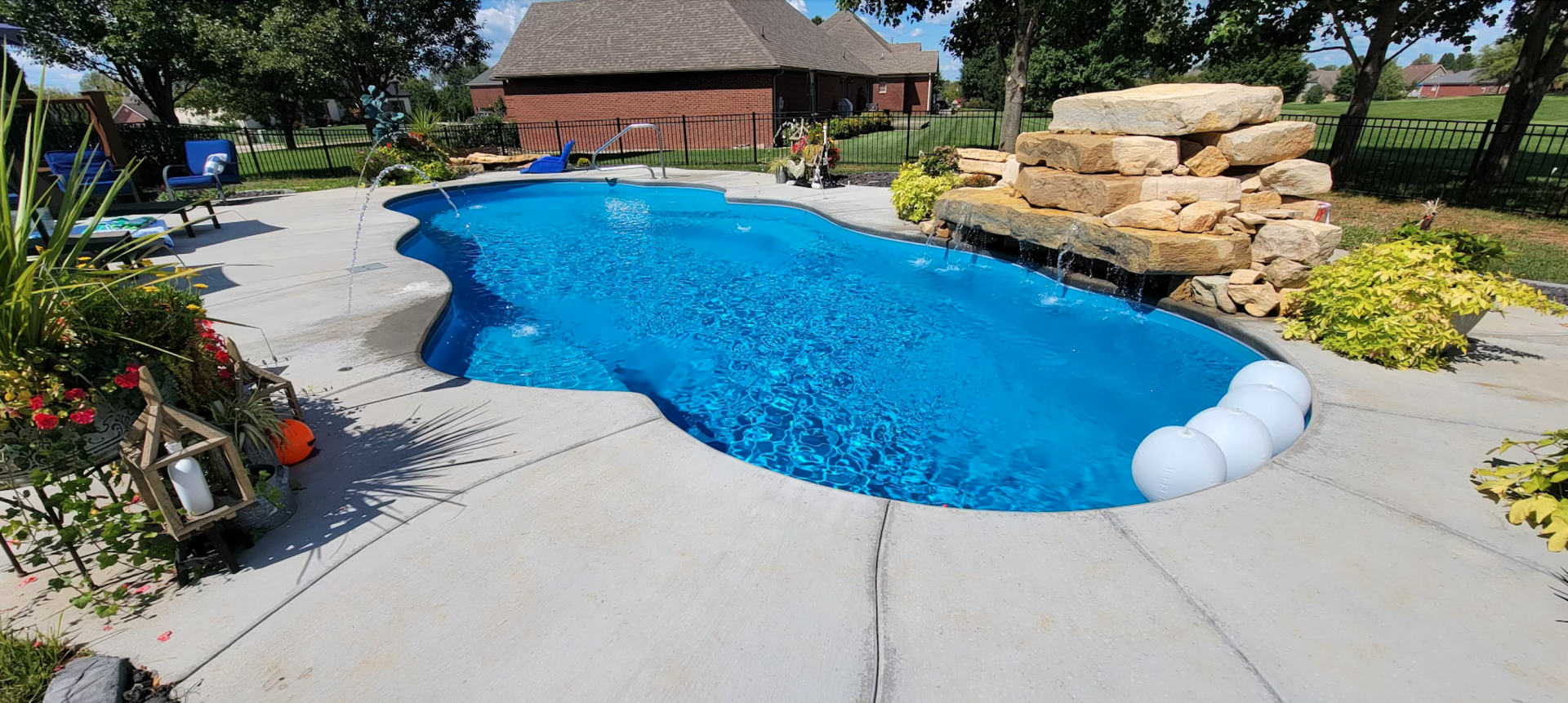 A large swimming pool with a waterfall in the backyard of a house.