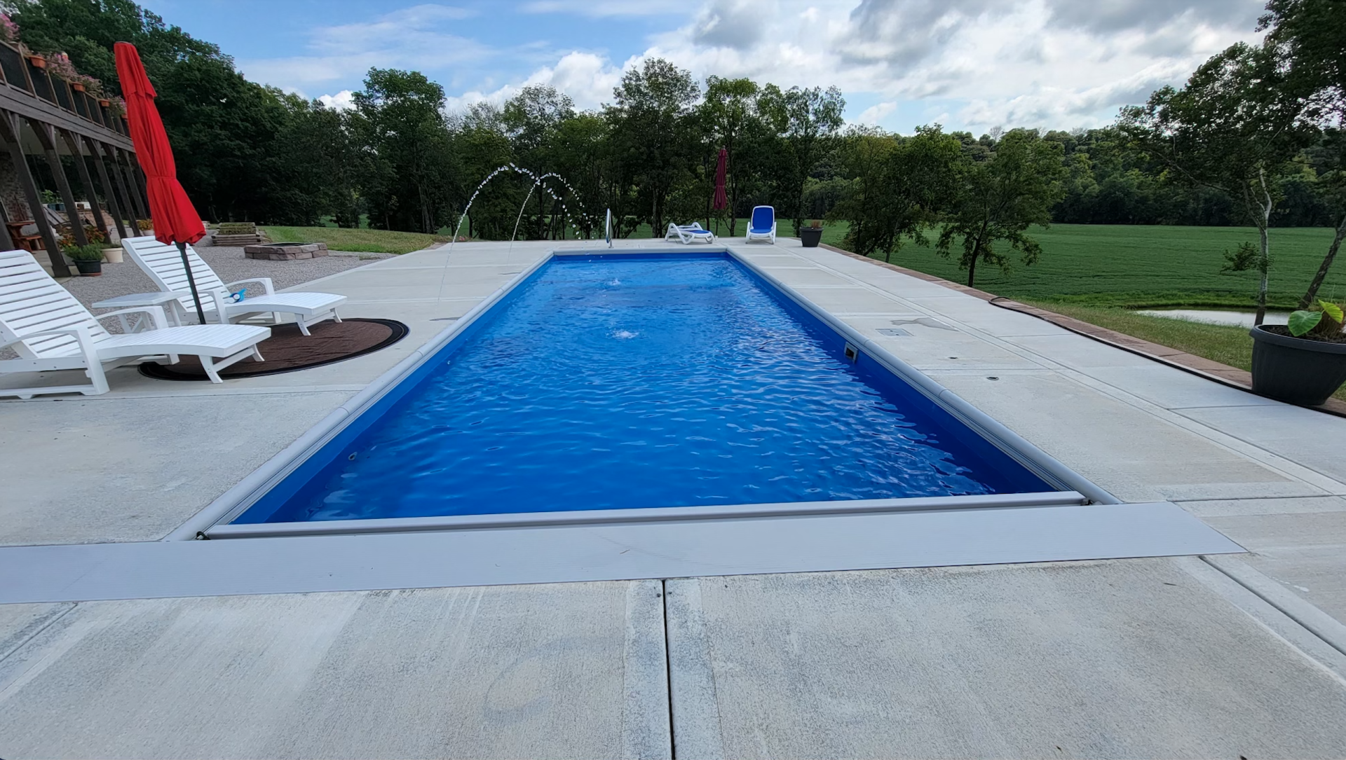 A large swimming pool surrounded by chairs and umbrellas in a backyard.