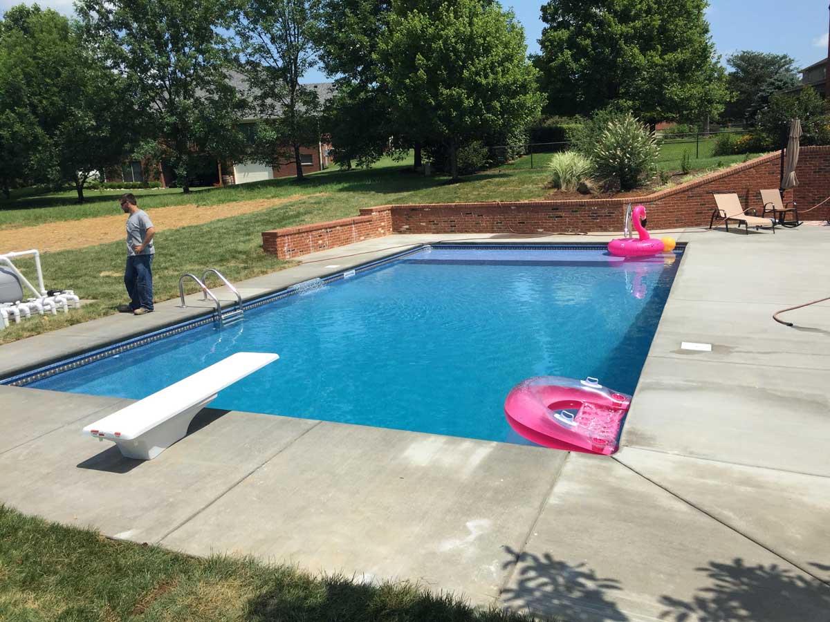A man is standing next to a large swimming pool.