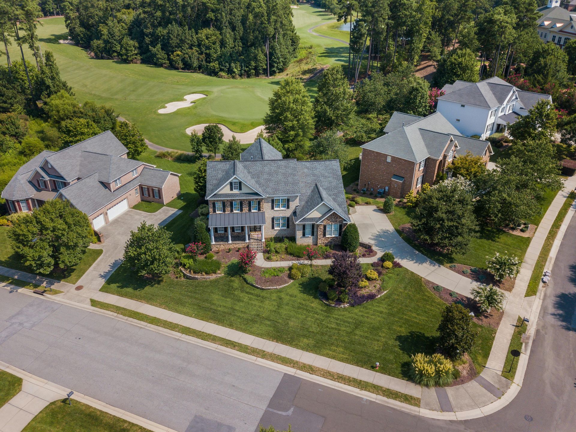 Aerial view of suburban houses with manicured lawns and a golf course in the background.
