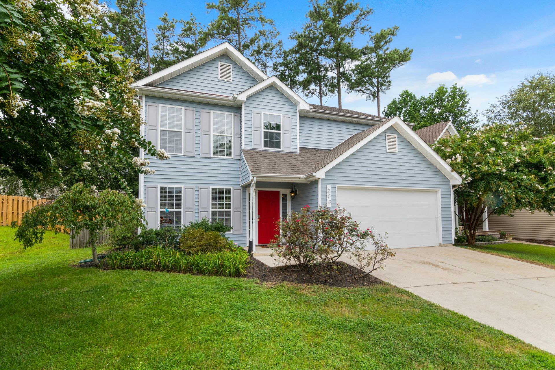 Blue two-story house with red door and white garage, surrounded by green lawn and trees.