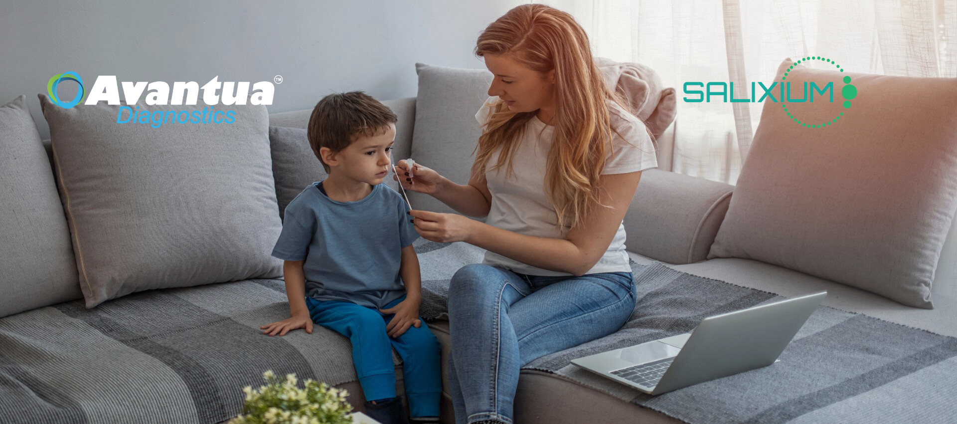 A woman is sitting on a couch with a child and a laptop.