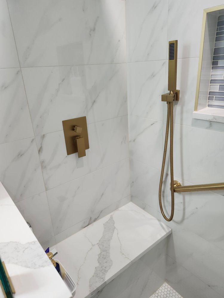 A bathroom with marble tiles and a gold shower head.