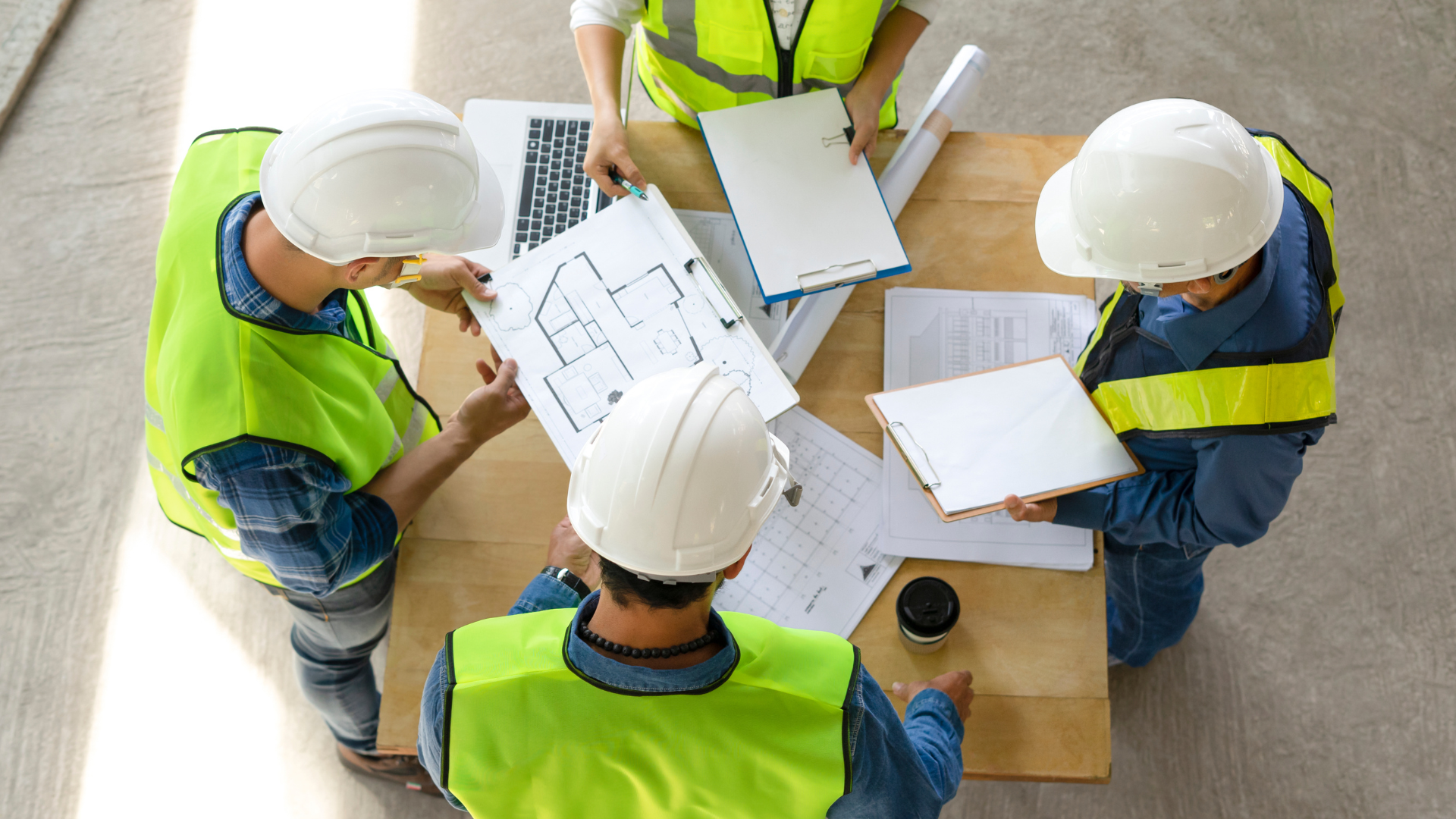 A group of construction workers are sitting around a table looking at a blueprint.