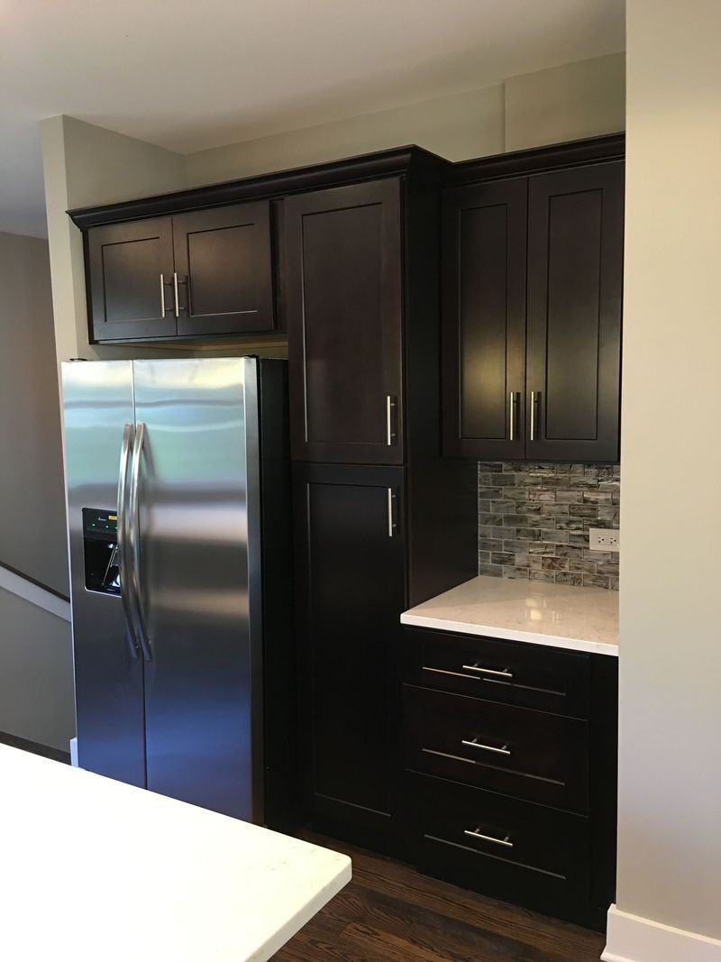 A kitchen with black cabinets and a stainless steel refrigerator.