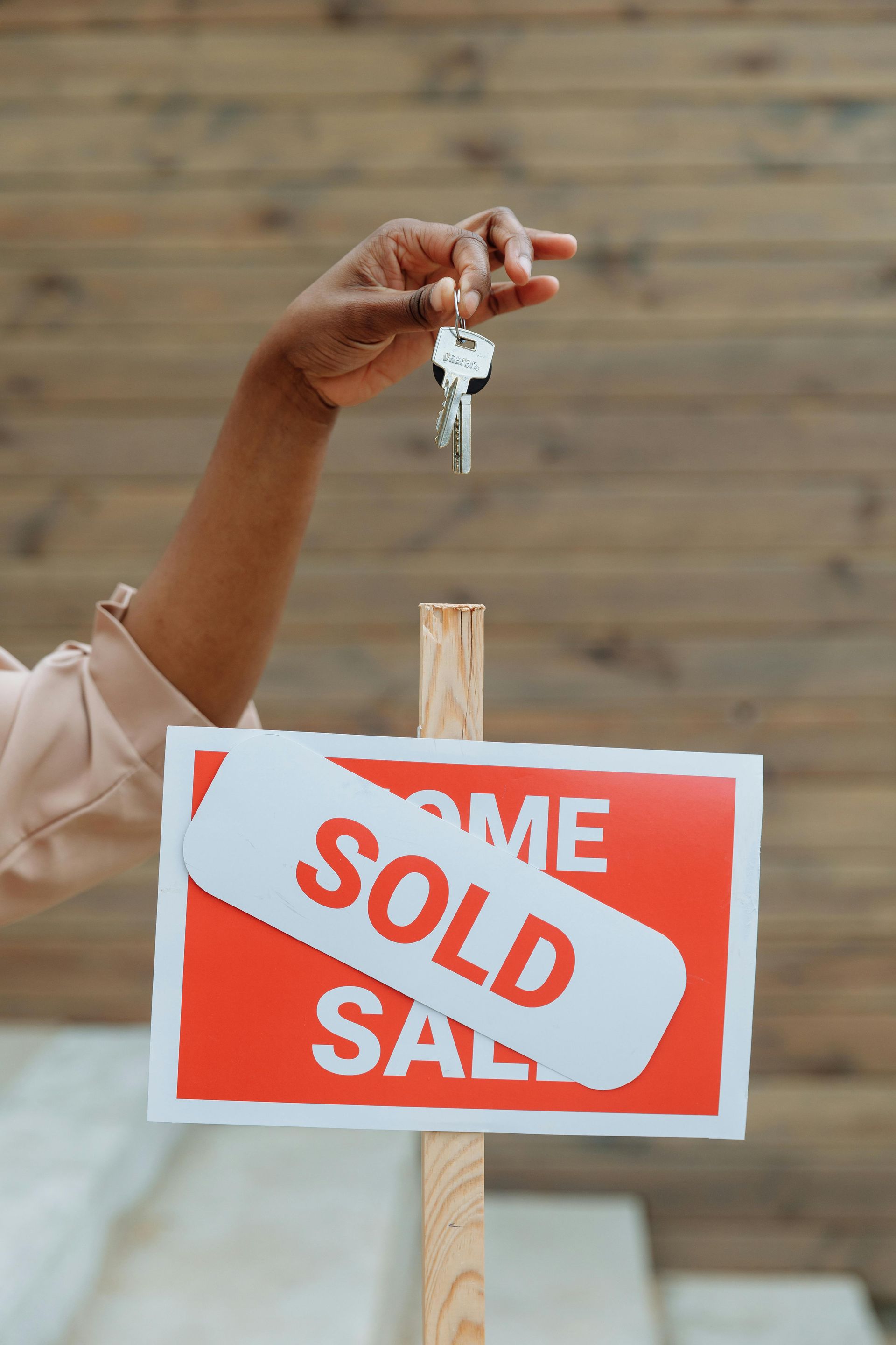 A person is holding a set of keys in front of a sold sign.