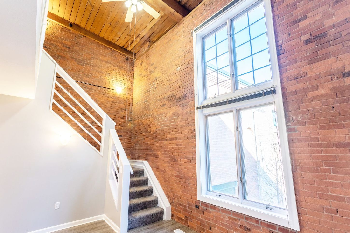 An empty room with a brick wall and stairs and a large window.