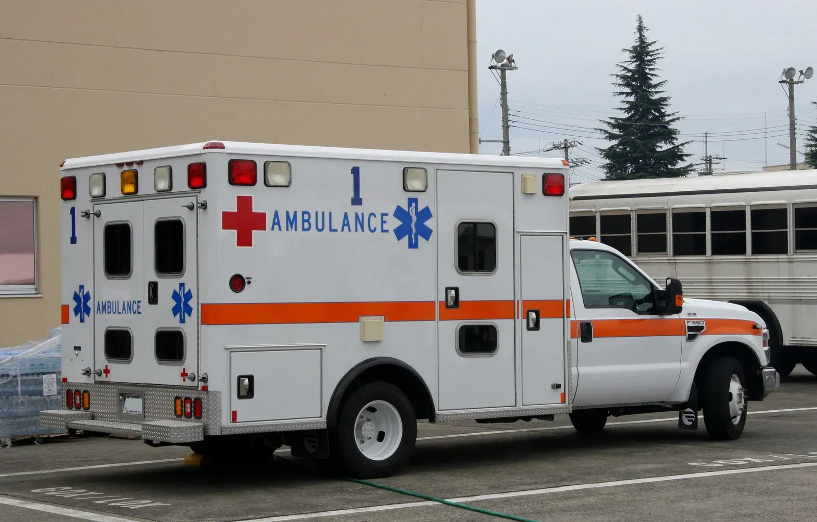 White ambulance parked outside a building, with red and blue emergency symbols and orange stripes.