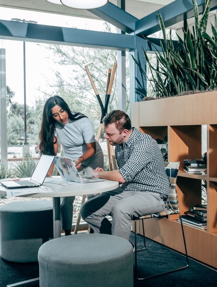 A man and a woman are sitting at a table looking at a laptop.