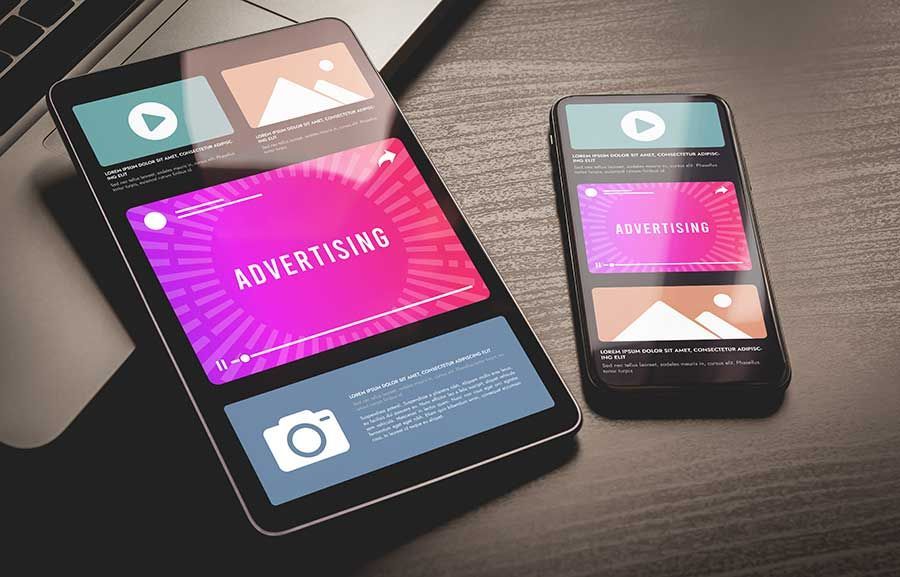 A tablet and a cell phone are sitting on a wooden table.