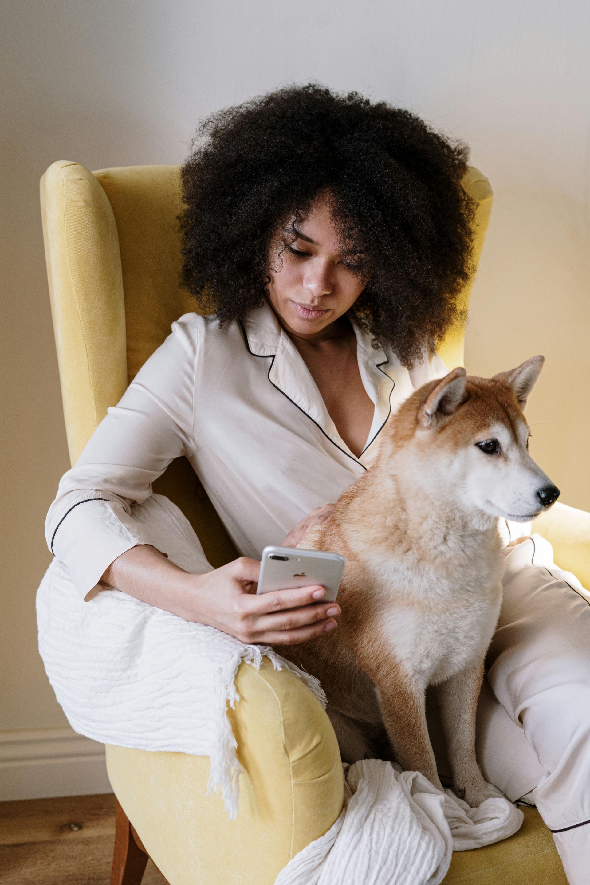 A woman is sitting in a chair with a dog and looking at her phone.