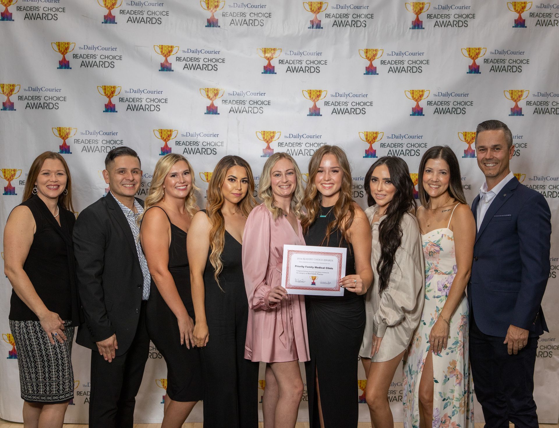 A group of people are posing for a picture in front of a wall with trophies on it.