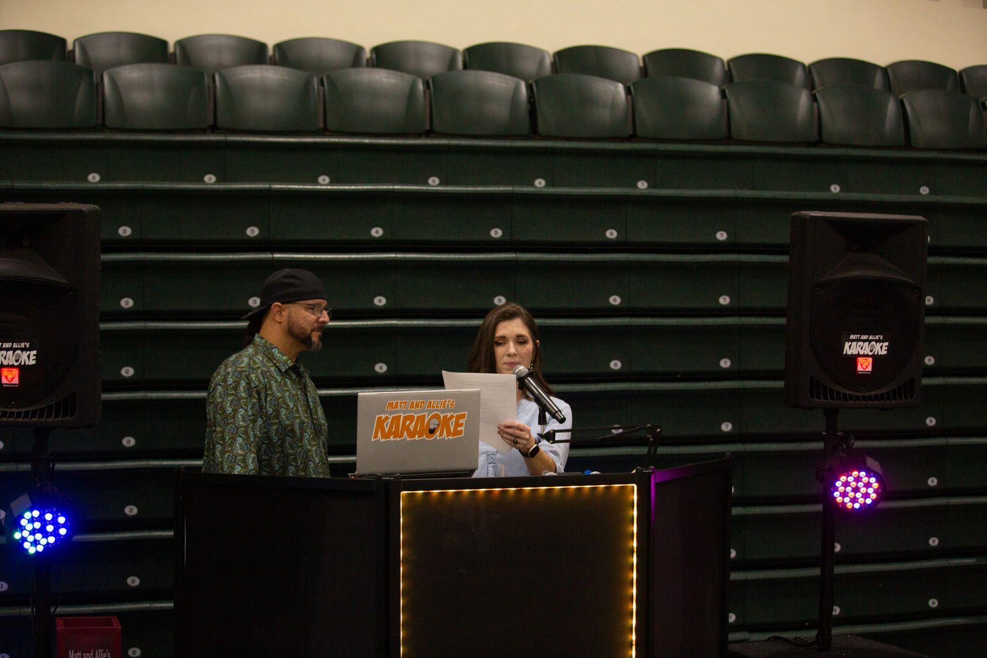 A man and a woman are standing in front of a dj booth in a stadium.