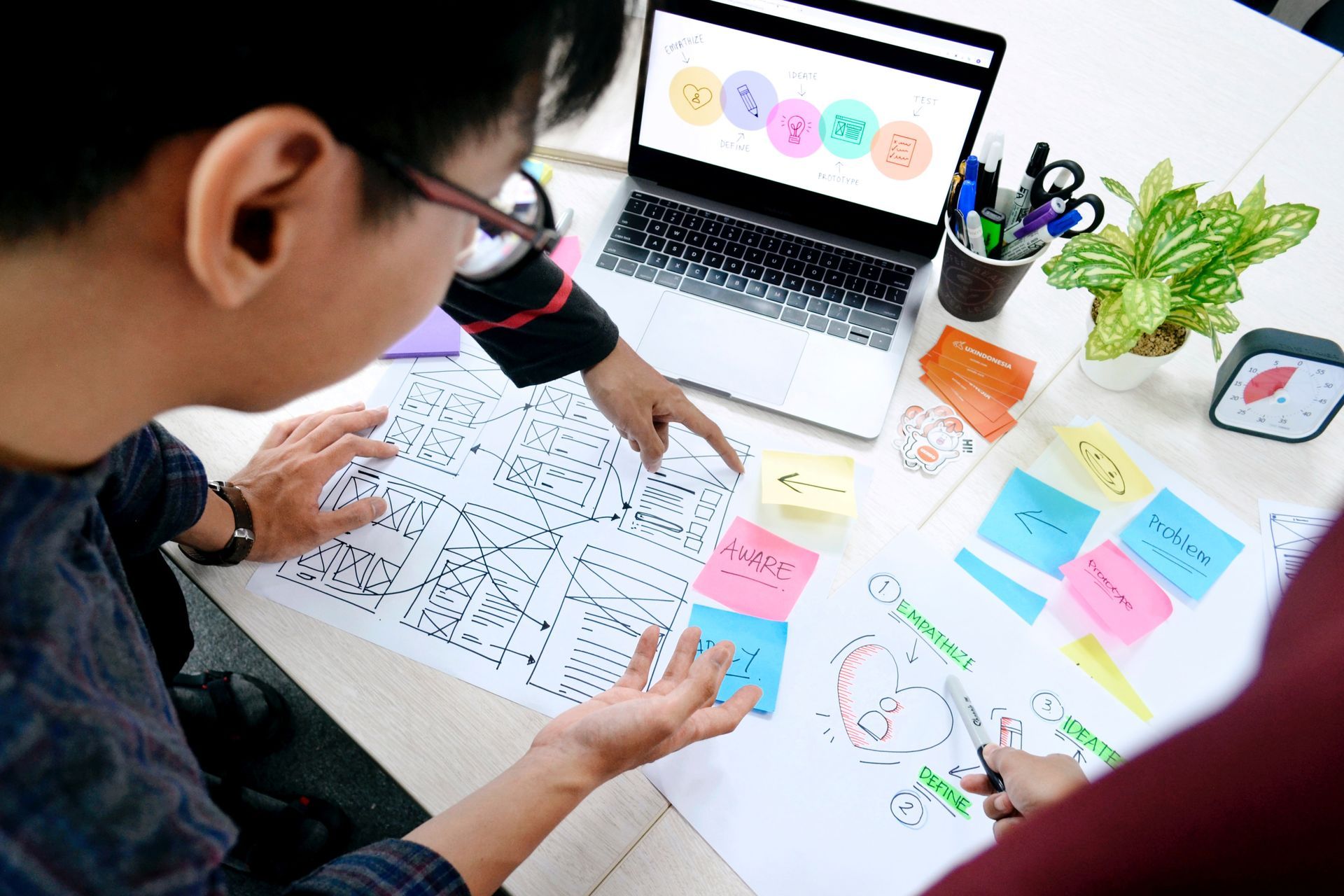 Two people are sitting at a table with a laptop and sticky notes.