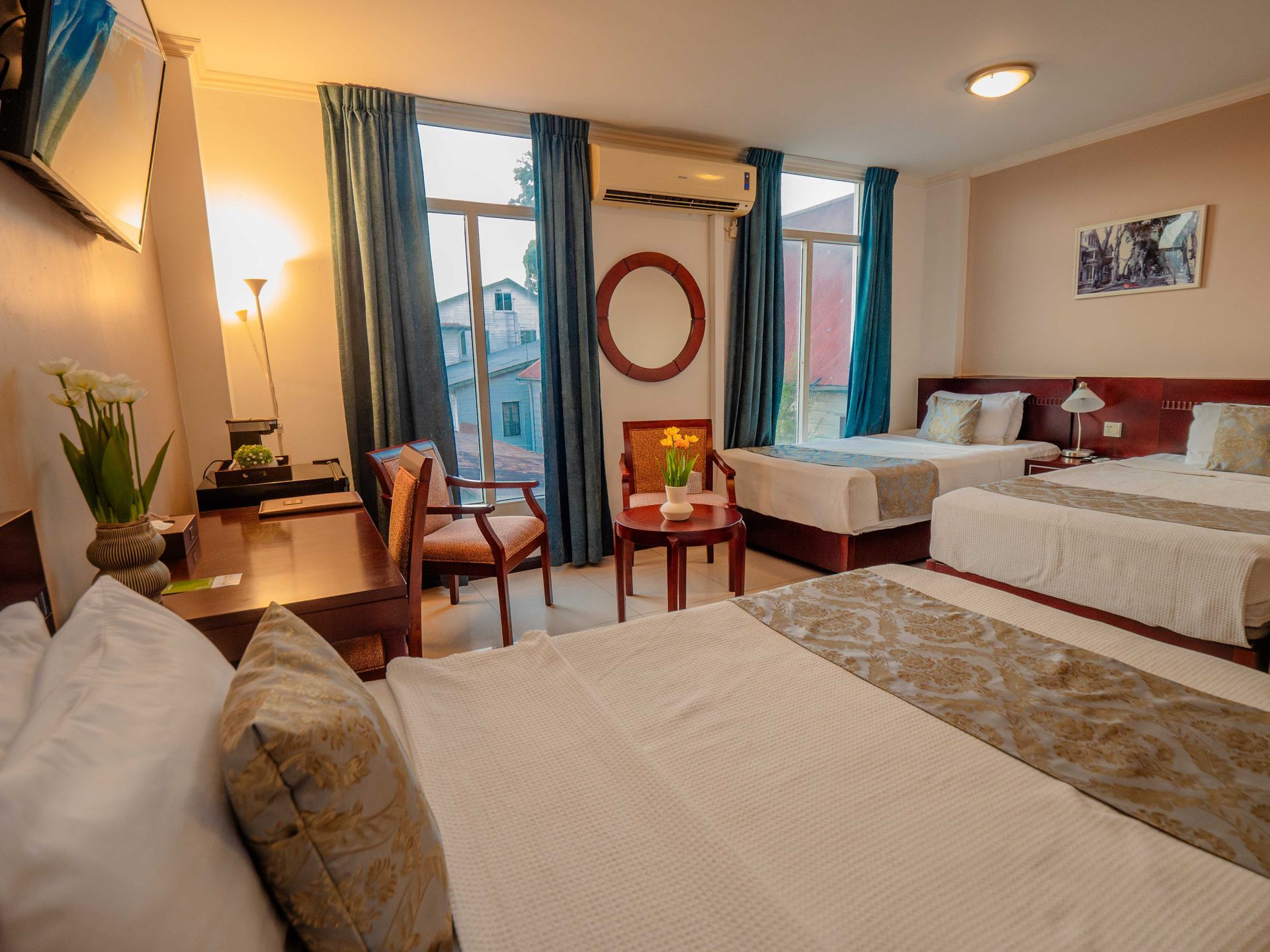 Hotel room with three beds, a sitting area, and a window with blue curtains.