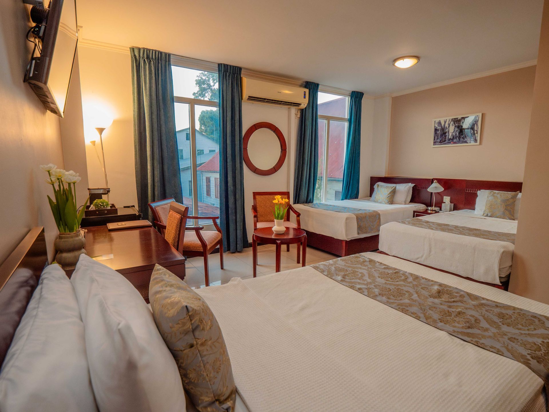 Hotel room with three beds, a seating area, and a window with blue curtains.