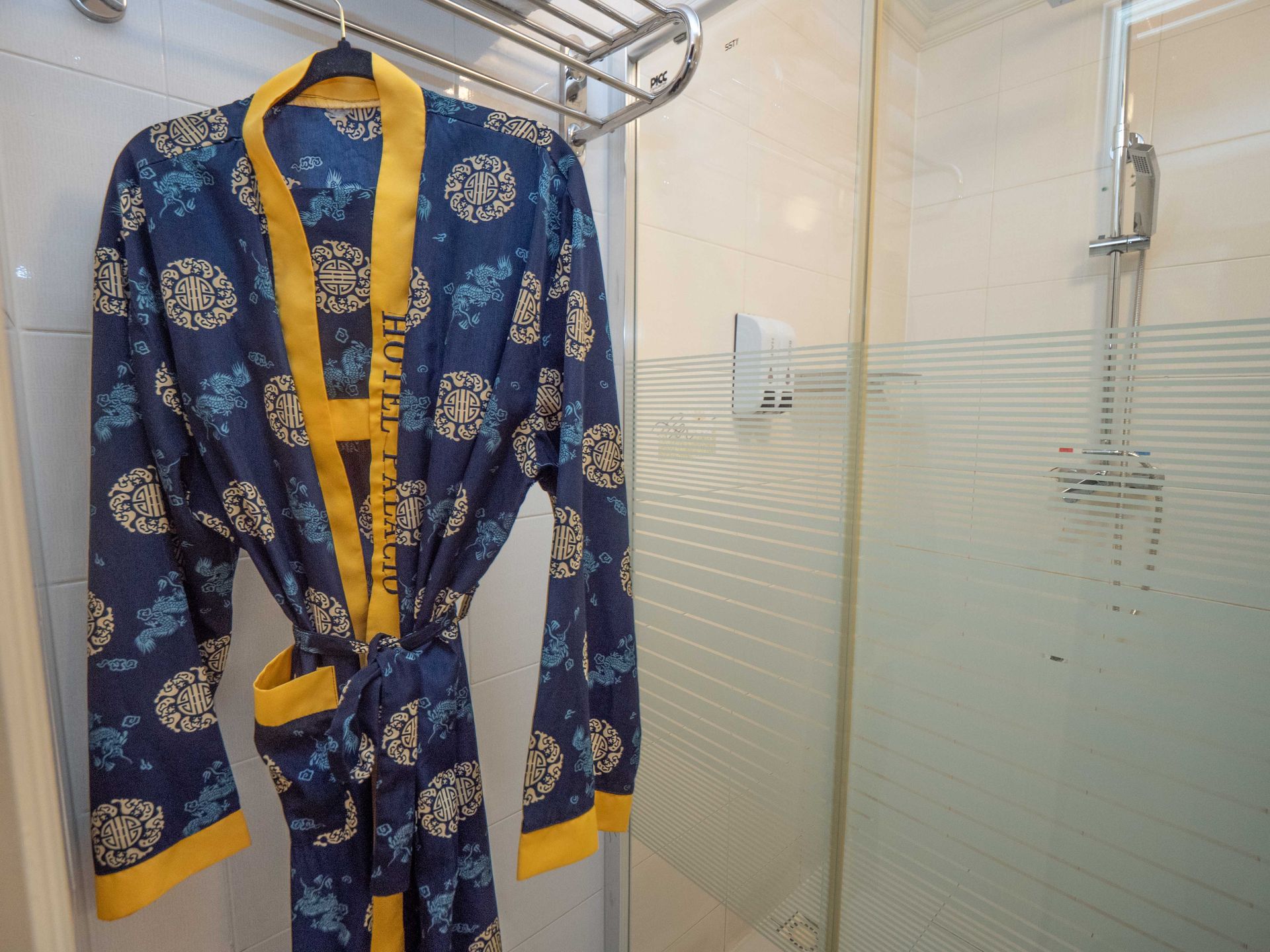 Blue and yellow patterned bathrobe hanging in a shower stall.