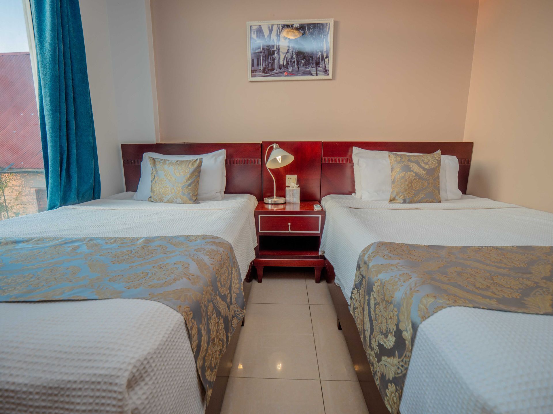 Two beds in a hotel room with white linens, gold accents, and a nightstand.