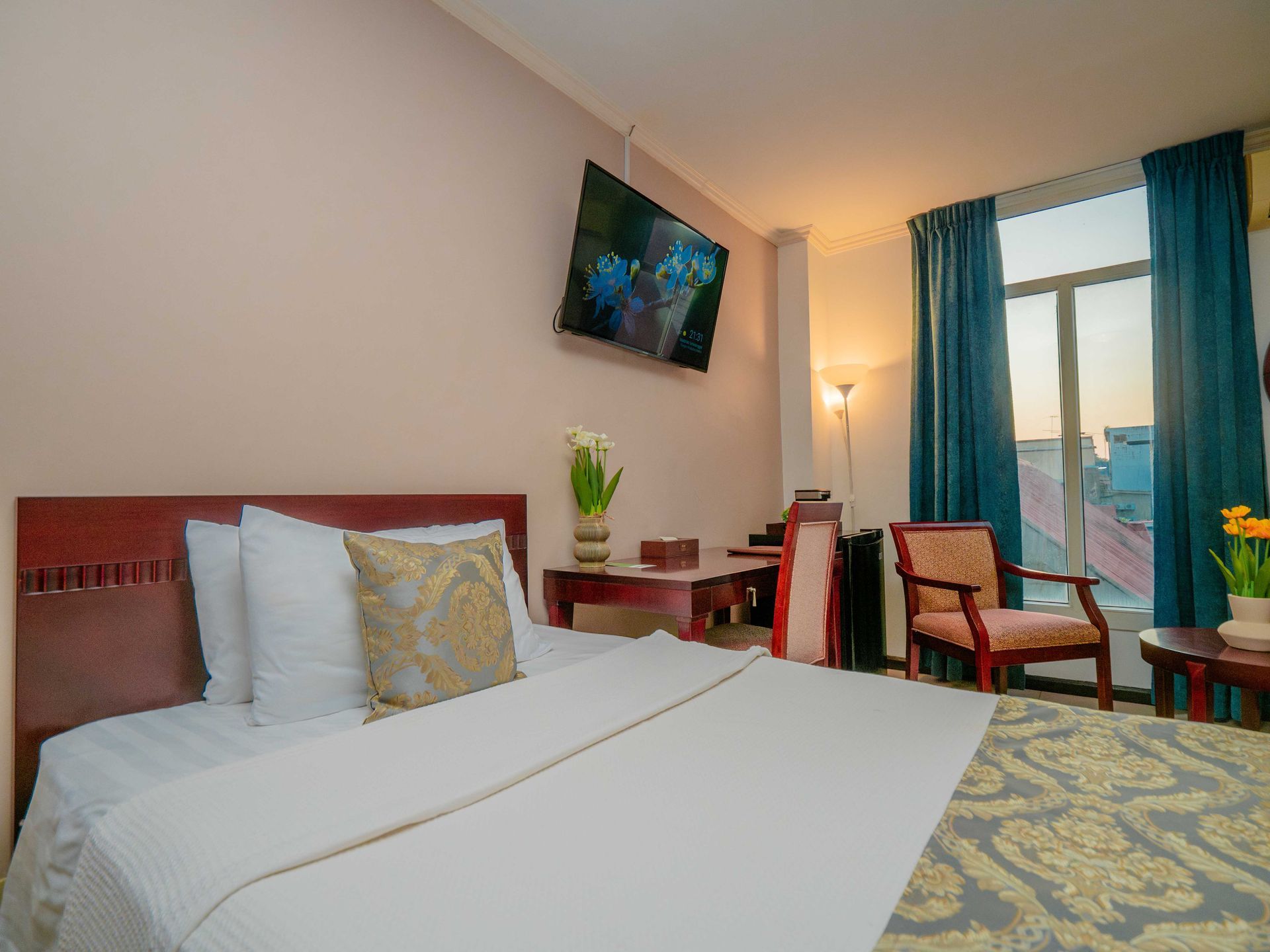 Hotel room with bed, TV, desk, chair, and window with blue curtains.