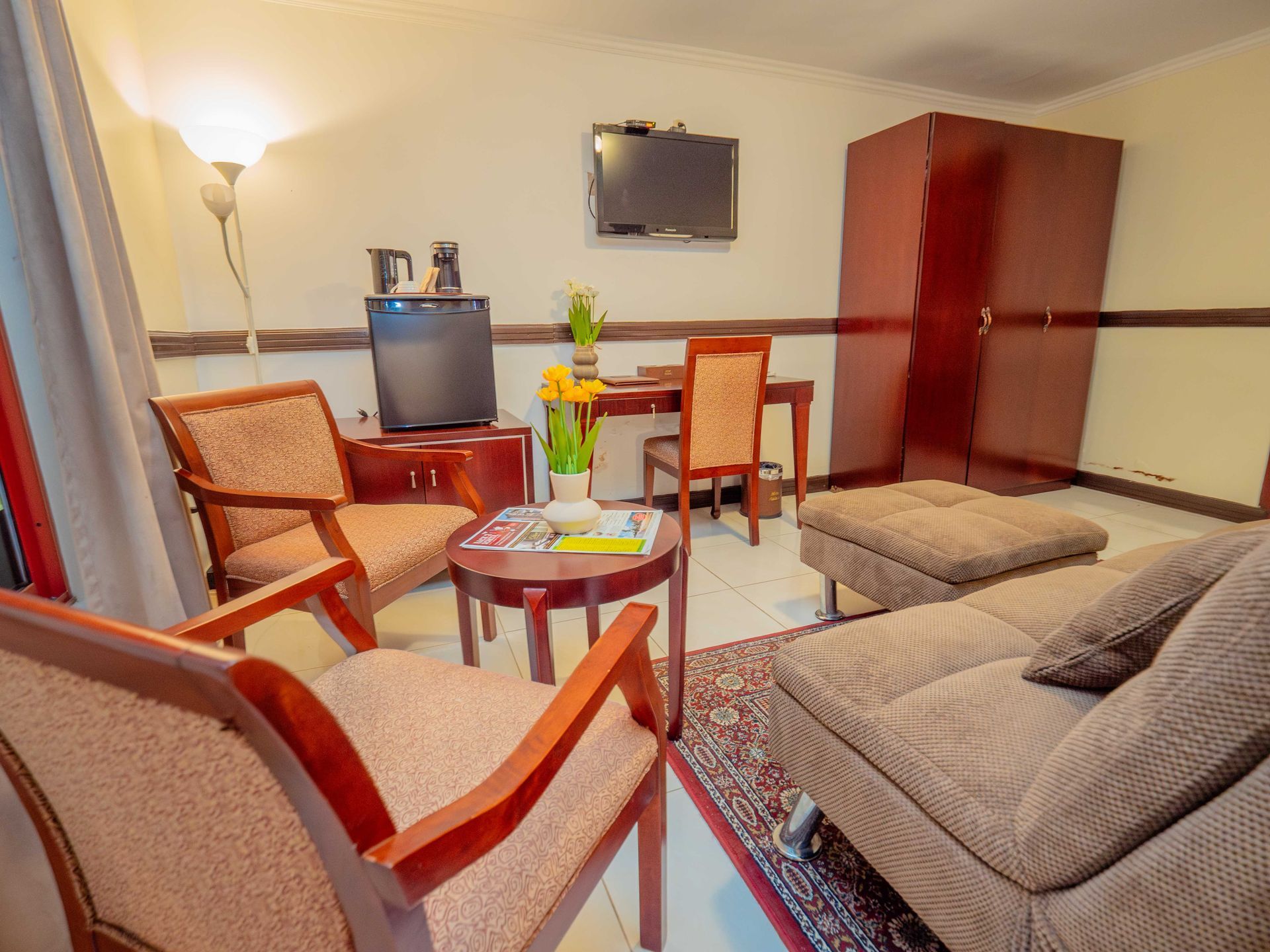 Hotel room: chairs, couch, table, TV, refrigerator, cabinet, hardwood floors.