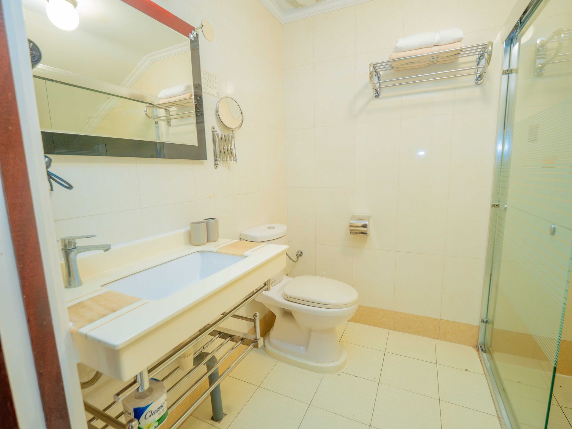 Bathroom with white sink, toilet, shower. Mirror above sink, towel rack.