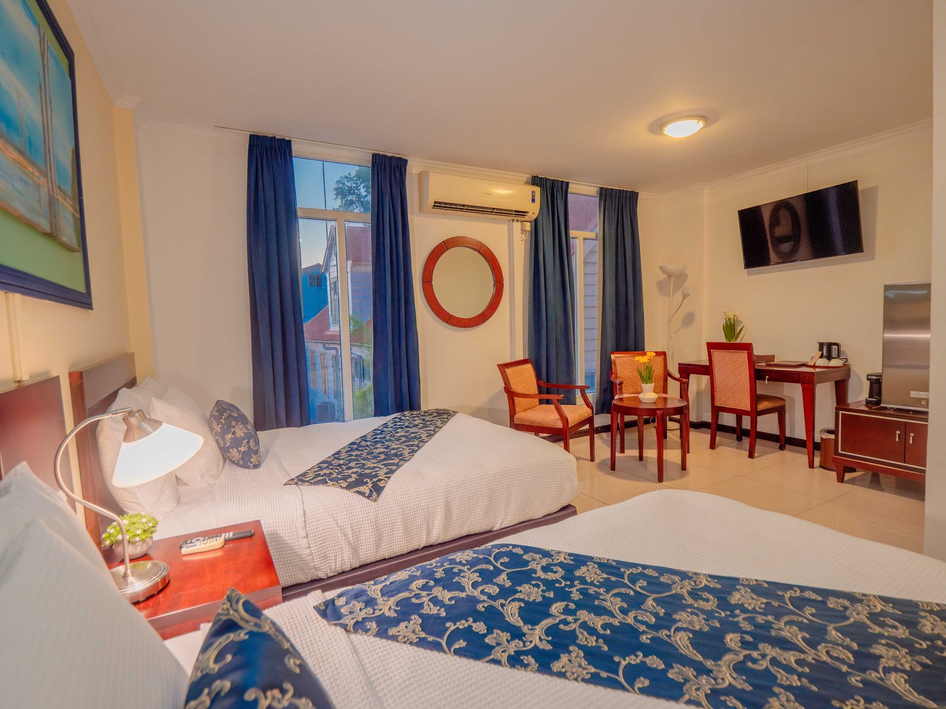 Hotel room with two beds, blue accents, TV, and a small dining area.