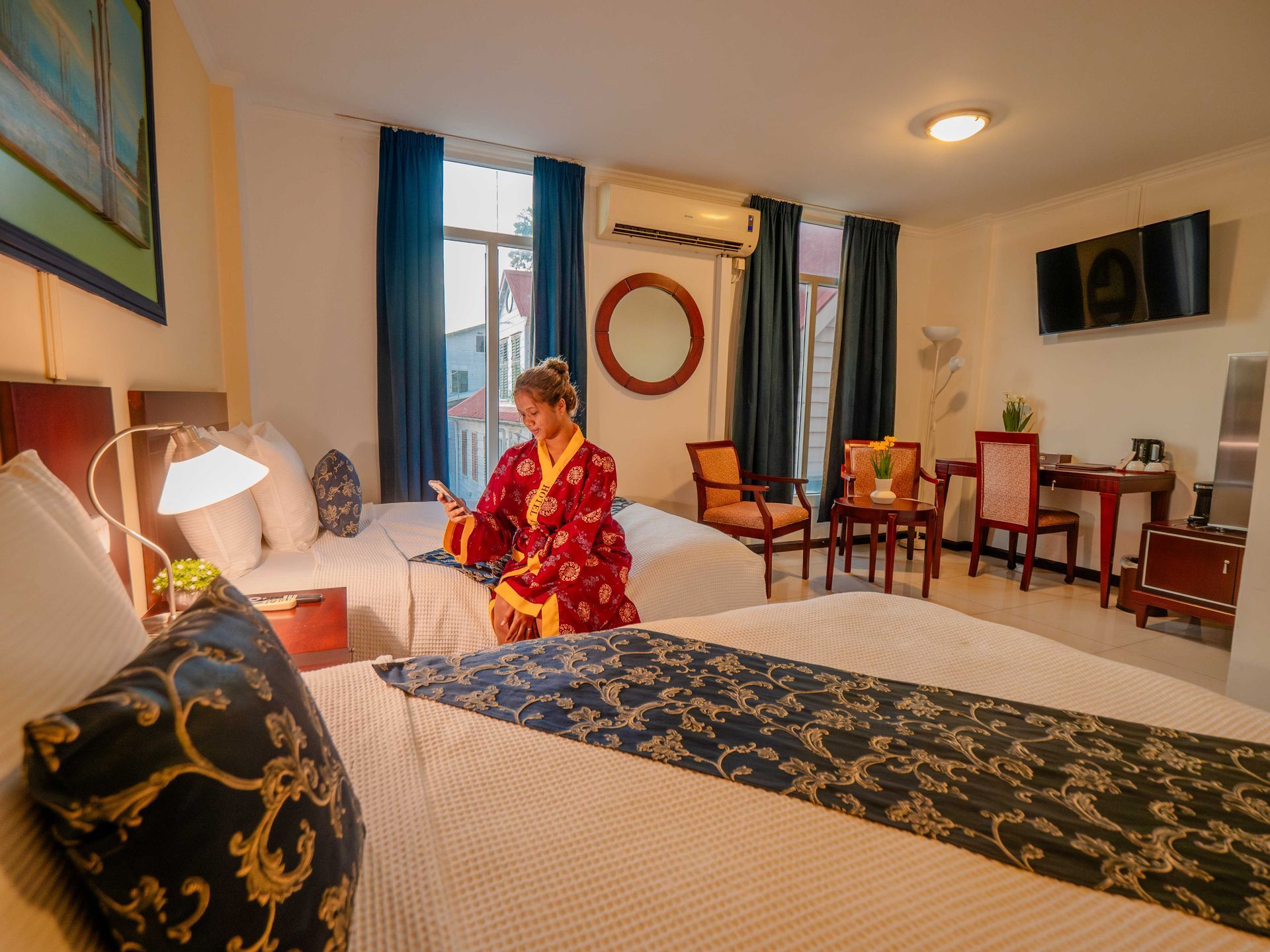 Woman in red robe uses phone in hotel room with two beds.