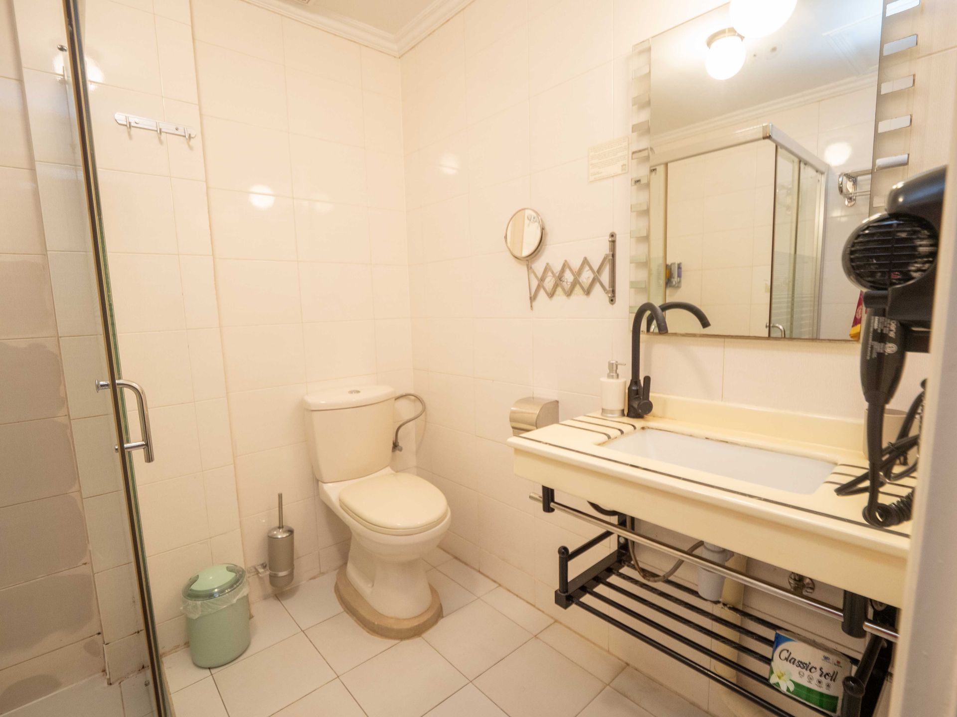 Bathroom with white tile, toilet, sink, mirror, and shower stall.