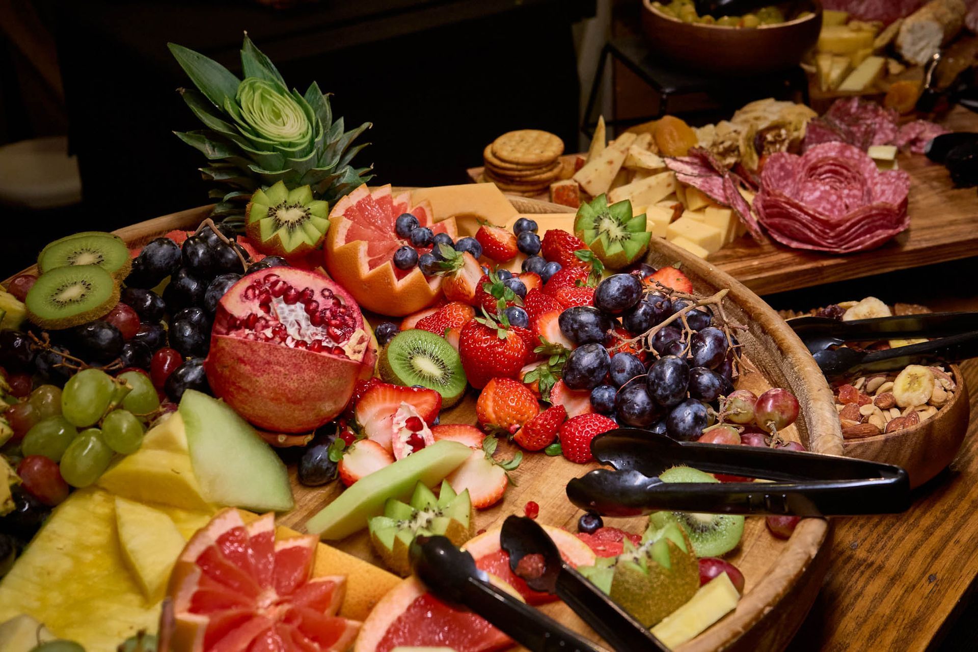 A wooden tray filled with fruit and tongs on a table.