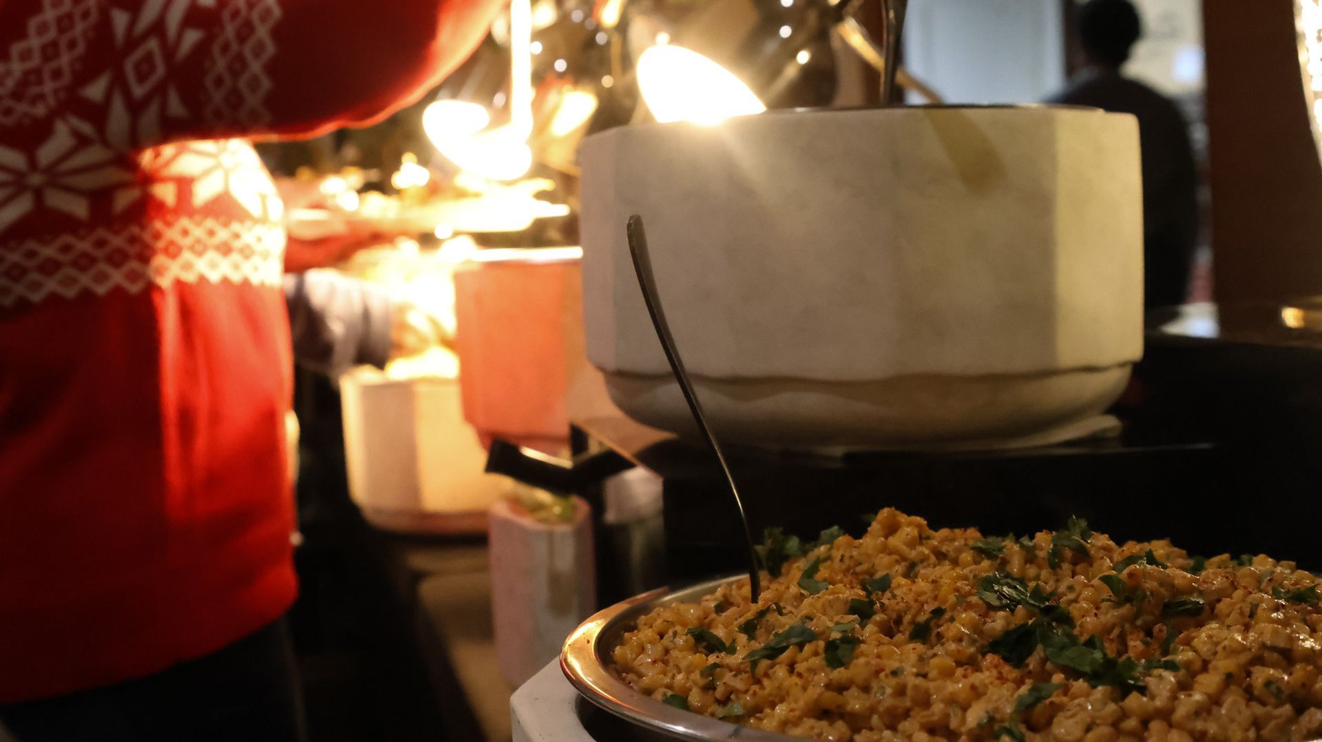 A person in a red sweater is standing next to a bowl of food.